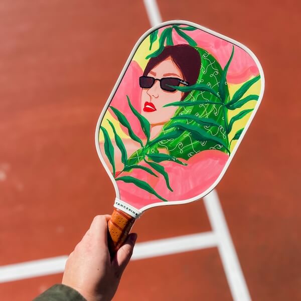 Holding a Tangerine pickleball paddle decorated with a woman wearing a scarf and sunglasses