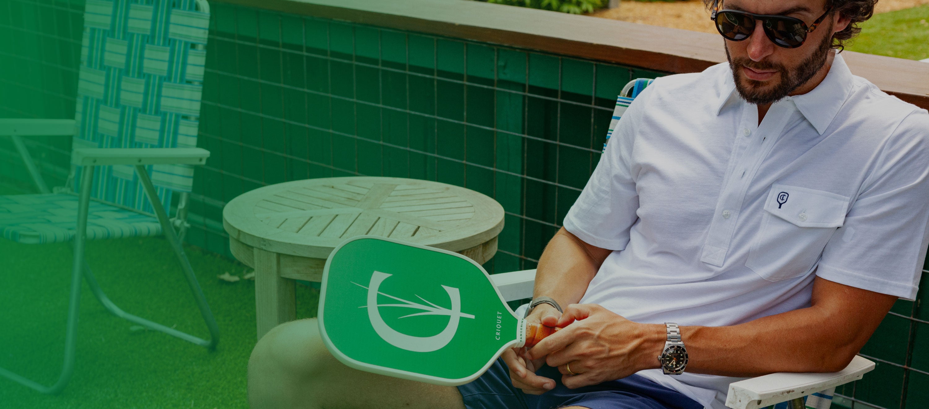 Man sitting and holding a green pickleball paddle with a C design
