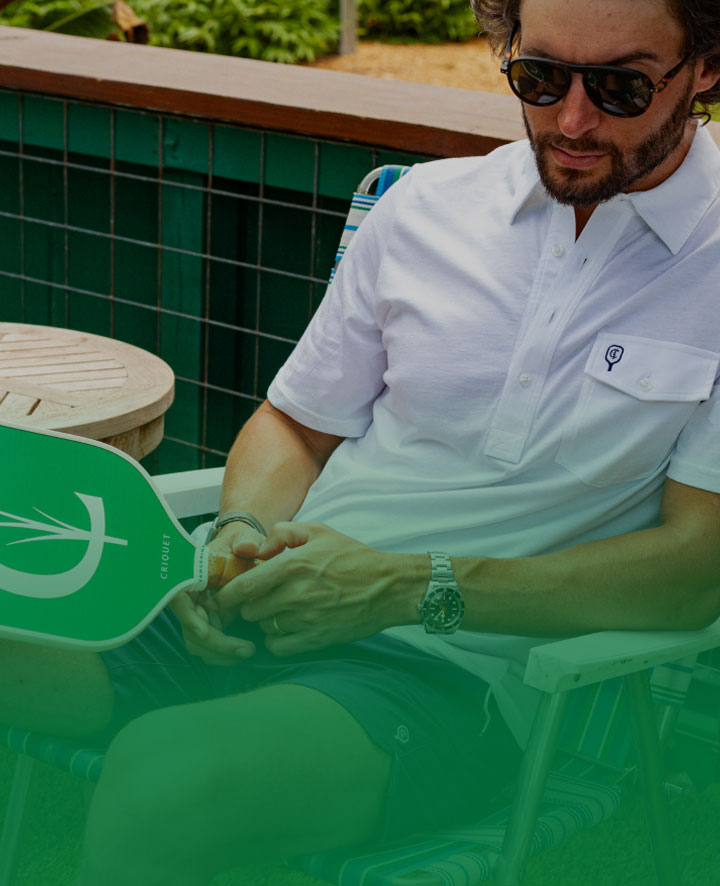 Man sitting and holding a green pickleball paddle with a C design