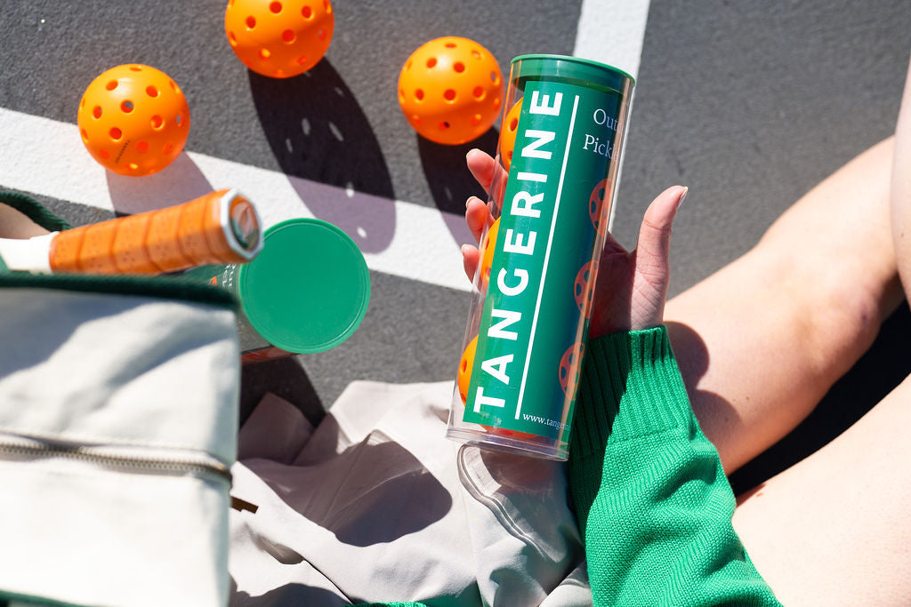 Pickleball player holding a container of Tangerine pickleball balls. 