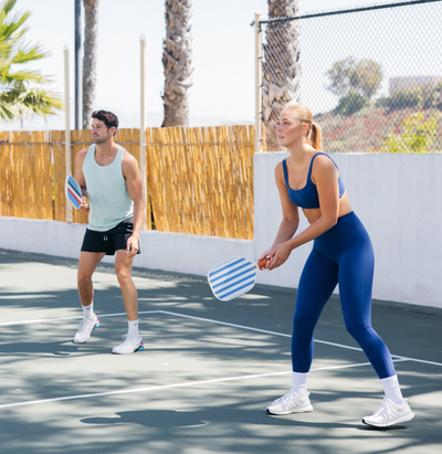 Girl and guy playing pickleball with colorful paddles. 