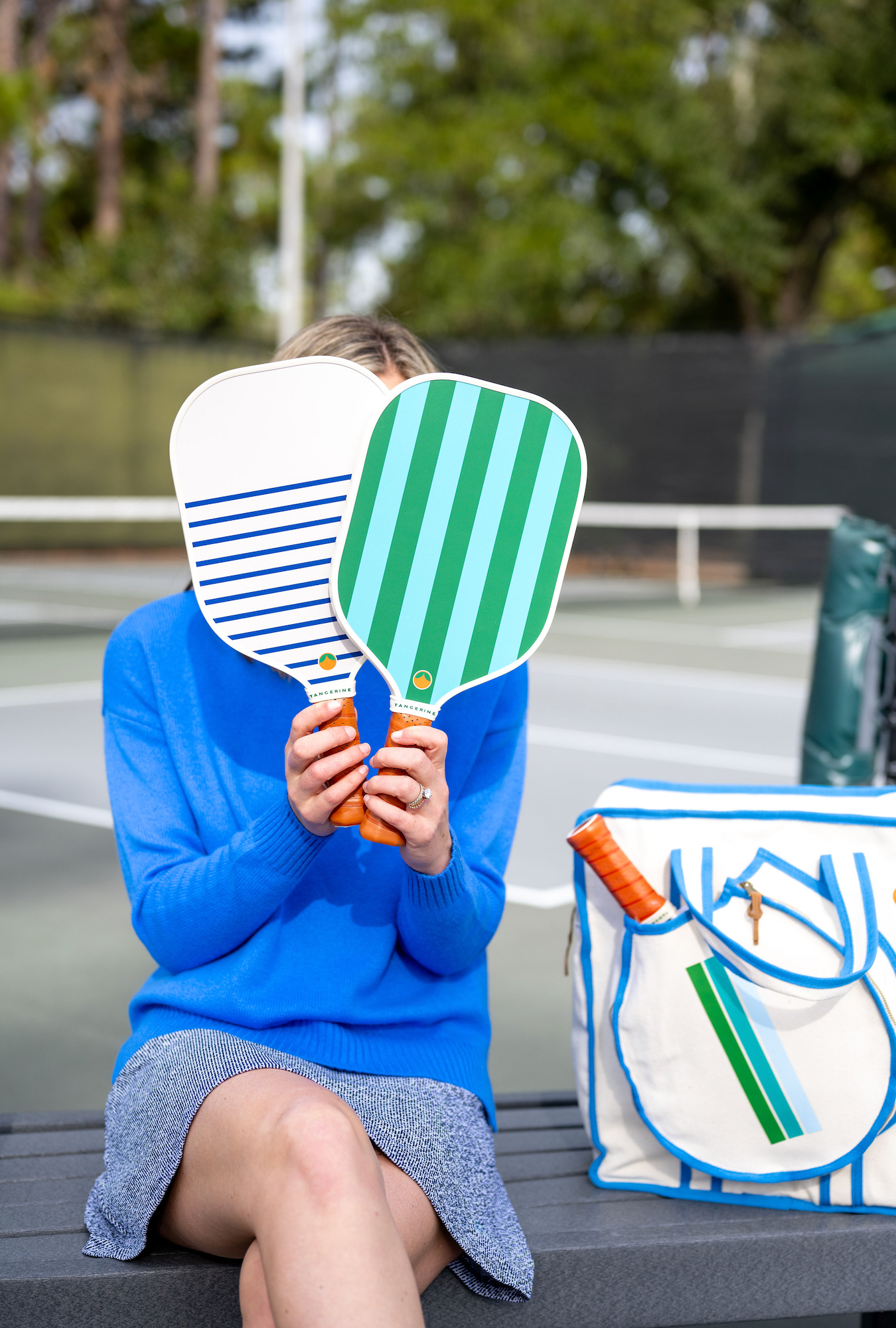 Woman holding two cute and colorful pickleball paddles alongside a blue bag
